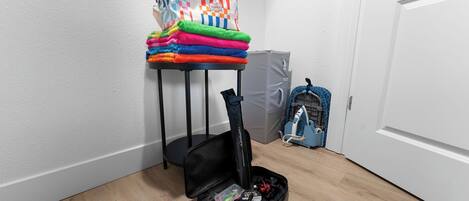 A room with a bed, a bedside table with a bag and folded clothes, a suitcase, and a vacuum cleaner.