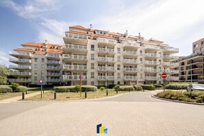 Um edifício residencial com vários andares, varandas, céu claro e placa de proibido estacionar.