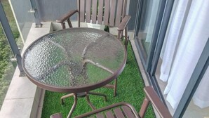 Un balcó amb una taula rodona de vidre i dues cadires metàl·liques, envoltat d'herba artificial.
