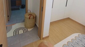 Habitació amb una porta de fusta que dona a un bany, una petita estora i un armari blanc.