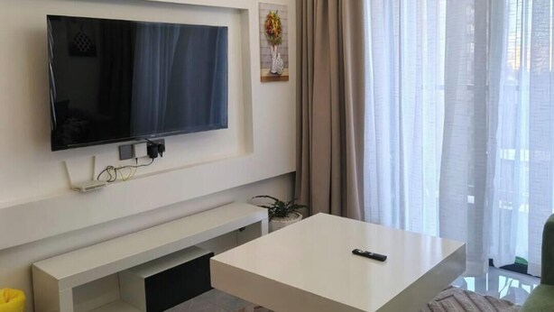 Un saló modern amb televisió de pantalla plana, una taula de cafè blanca i una finestra gran amb cortines.