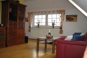 A living room with a red sofa, wooden cabinet, and a table with a bottle. - Holiday apartment with 1 bedroom (Norderney)