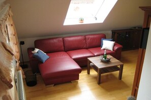 A red leather sofa with a wooden coffee table, a small potted plant, and a skylight above. - Holiday apartment with 1 bedroom (Norderney)