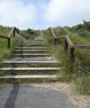 A set of outdoor stone steps with wooden railings, surrounded by grass and shrubs. - Holiday apartment with 1 bedroom (Norderney)