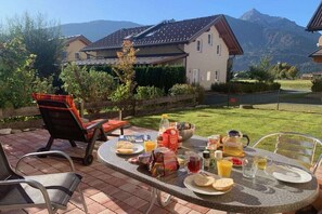 Eine Terrasse mit Frühstückstisch, umgeben von einem Holzzaun, mit Blick auf die Berge im Hintergrund.