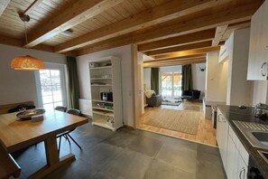 Eine moderne Küche mit Holzbalkendecke, ein Essbereich mit Tisch und Stühlen und Blick in ein Wohnzimmer.
