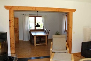 Ein Zimmer mit Holzbalken, einem Esstisch, Stühlen, einer Couch und einem schwarzen Sessel.