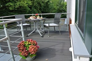 Ein Balkon mit Tisch, Stühlen, einer Topfpflanze und einem Geländer.