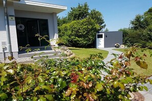 Ein modernes Gebäude mit weißer Fassade, einer kleinen Veranda und einem gepflegten Rasen.