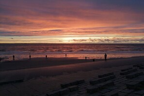 Ein Strand bei Sonnenuntergang, Menschen sind unterwegs und Stufen führen zum Wasser.