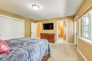 Ein Schlafzimmer mit Bett, Kommode, Fernseher und einer Tür zu einem anderen Raum.