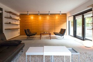 Ein modernes Wohnzimmer mit einer Couch, zwei Sesseln, einem Couchtisch und einem weißen Beistelltisch.