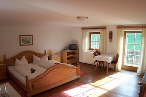 Ein Schlafzimmer mit einem hölzernen Bett, einem Schreibtisch, einem Stuhl, einem Fernseher und einem Fenster mit Vorhängen.