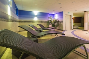 Ein Wellnessbereich mit Liegestühlen, einer Wand mit Strukturmuster und einer Topfpflanze.