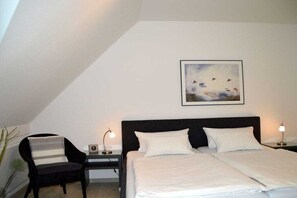Un dormitorio con una cama, dos mesitas de noche con lámparas, una silla y un cuadro en la pared.