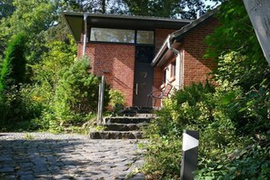 Ein Backsteinhaus mit einer Tür und Stufen, umgeben von viel Grün.