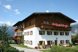 Eine zweistöckige Chalet mit Holzbalkonen, einem geneigten Dach und einem Berg im Hintergrund.