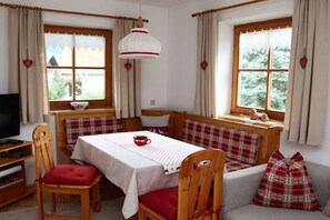 Ein gemütliches Zimmer mit einer hölzernen Bank, einem Tisch mit weißem Tuch und einem Fernseher.