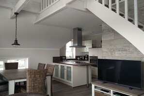 Eine moderne Küche mit einer großen Kochinsel, ein Essbereich mit Korbstühlen, einem Flachbildfernseher und einer Treppe.