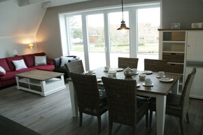 Ein Essbereich mit einem für vier Personen gedeckten Tisch, umgeben von Korbstühlen, einem roten Sofa und einer weißen Kommode.