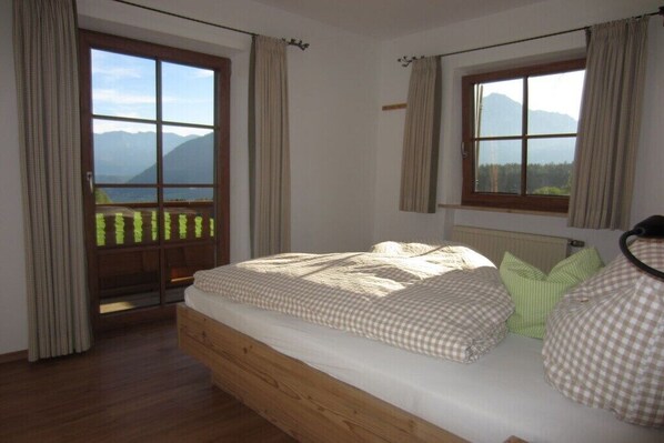 A bedroom with a wooden bed, a view of mountains through a large window, and a balcony with curtains.