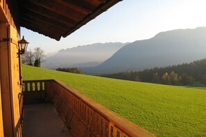 A wooden balcony with a view of a green field and mountains.