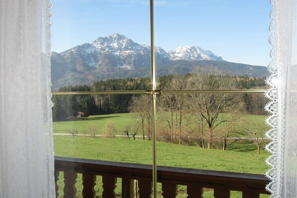 A view from a balcony with a metal railing, a mountain range in the background, and a green field in the foreground.