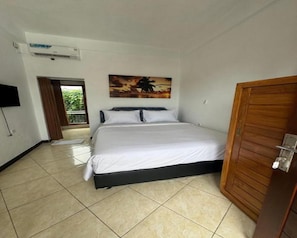 Quarto com cama, televisão, quadro e porta de madeira.