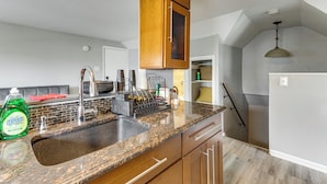Una cocina con encimeras de granito, armarios de madera, pileta de acero inoxidable y una lámpara colgante.