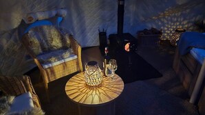 Ein gemütliches Zimmer mit einem runden Tisch, Korbstühlen, einem Glas und einer Kerze.
