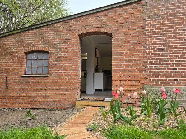 A brick building with a small window and an archway entrance, leading into a kitchen area.