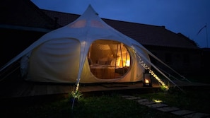 Une tente avec un lit à l’intérieur, une lanterne à l’extérieur et un bâtiment en briques en arrière-plan.