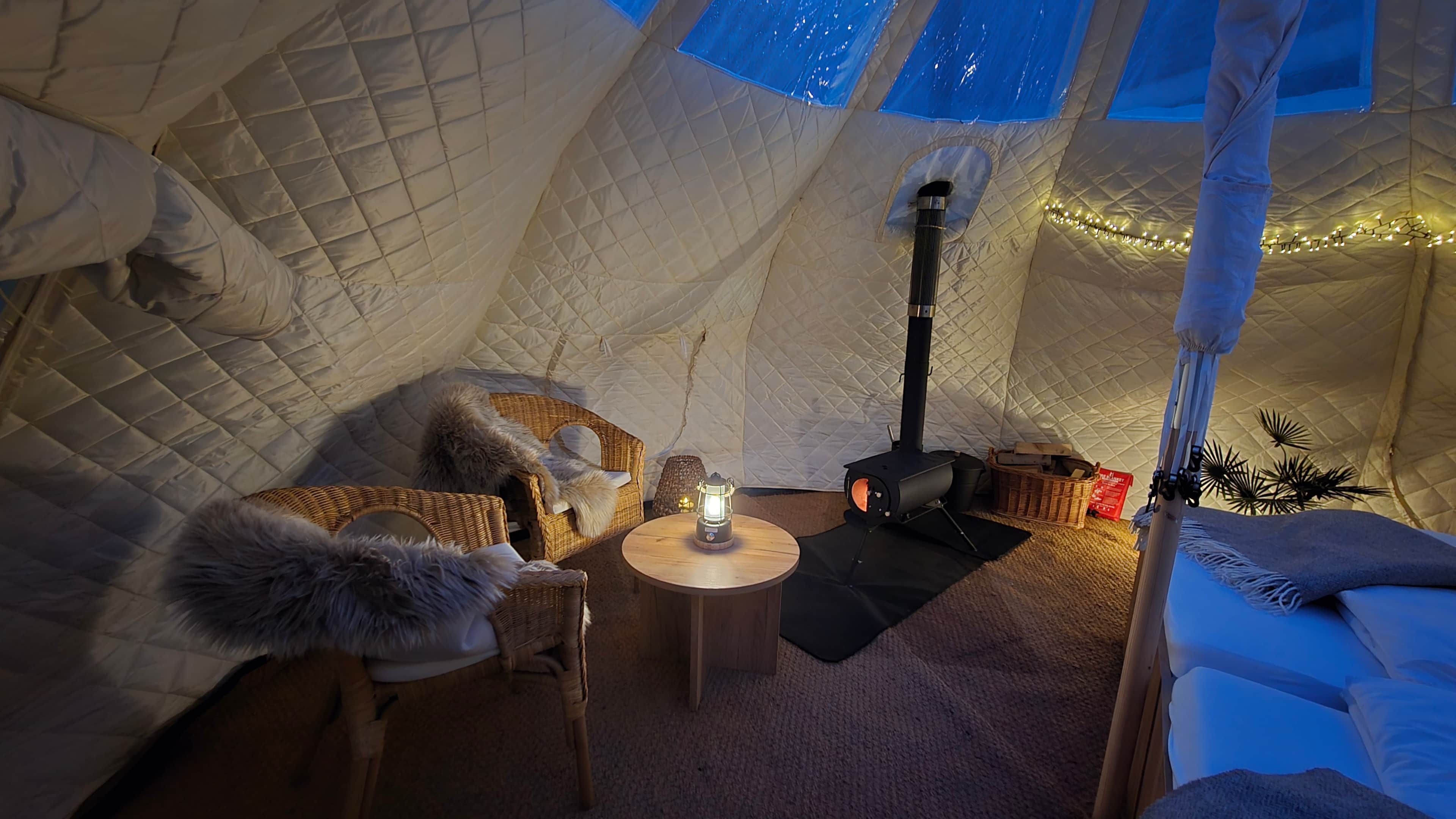 A cozy interior of a tent with a central table, a portable stove, and a comfortable seating area.
