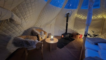 A cozy interior of a tent with a central table, a portable stove, and a comfortable seating area.