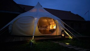 Ein Zelt mit einem Bett im Inneren, eine Laterne davor und ein Backsteinhaus im Hintergrund.