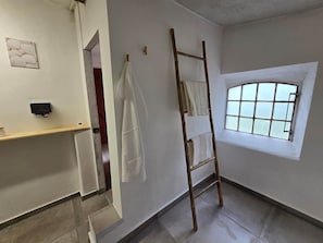 A room with a wooden ladder, a window with frosted glass, a towel rack, and a door leading to another room.