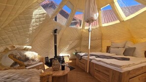 Ein gemütliches Zelt-ähnliches Zimmer mit einem Bett, einem Sessel, einem Tisch mit einer Flasche und einer kleinen Tischlampe.