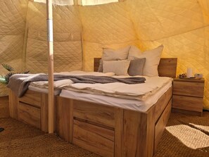 Ein Zeltraum mit Bett, Holzkasten, Nachttisch und kleinem Tisch.