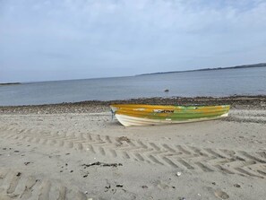 A boat on a sandy beach with a calm sea in the background.