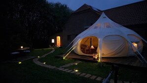 Et telt med træterrasse, en stol og et bord indeni, omgivet af en murbygning og en sti.