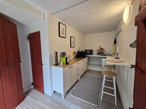 A compact kitchen with white cabinets, a microwave, a sink, and a small dining area with stools.