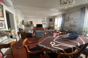 A dining area with a table, chairs, a sofa, a television, and a chandelier. - Beautiful Central Apartment in Montpellier (Montpellier)