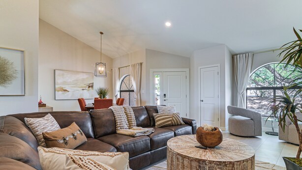A modern living room with a leather sofa, a round coffee table, and a large window with curtains. - Mtn-View Fountain Hills Oasis w/ Private Pool! (Fountain Hills)