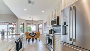 A modern kitchen with stainless steel appliances, a dining area with chairs, and a view through the window. - Mtn-View Fountain Hills Oasis w/ Private Pool! (Fountain Hills)
