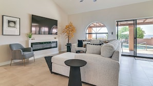 A modern living room with a sofa, armchair, TV, fireplace, and a large window. - Mtn-View Fountain Hills Oasis w/ Private Pool! (Fountain Hills)