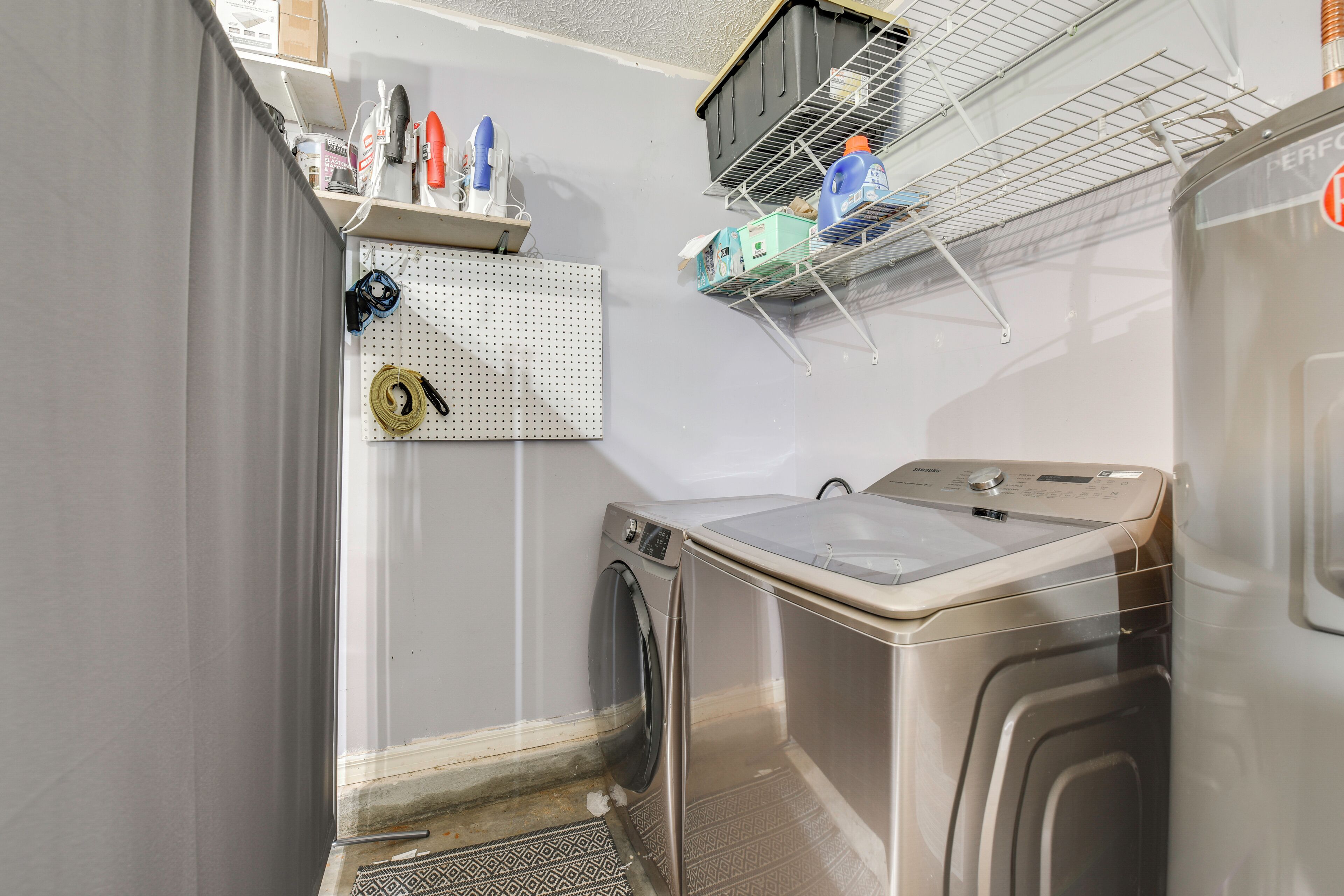 A laundry room with a washing machine, a drying rack, and a pegboard with various items.