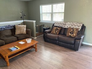 Ein Wohnzimmer mit zwei Sofas, einem Holztisch und einem Fenster mit Jalousien.
