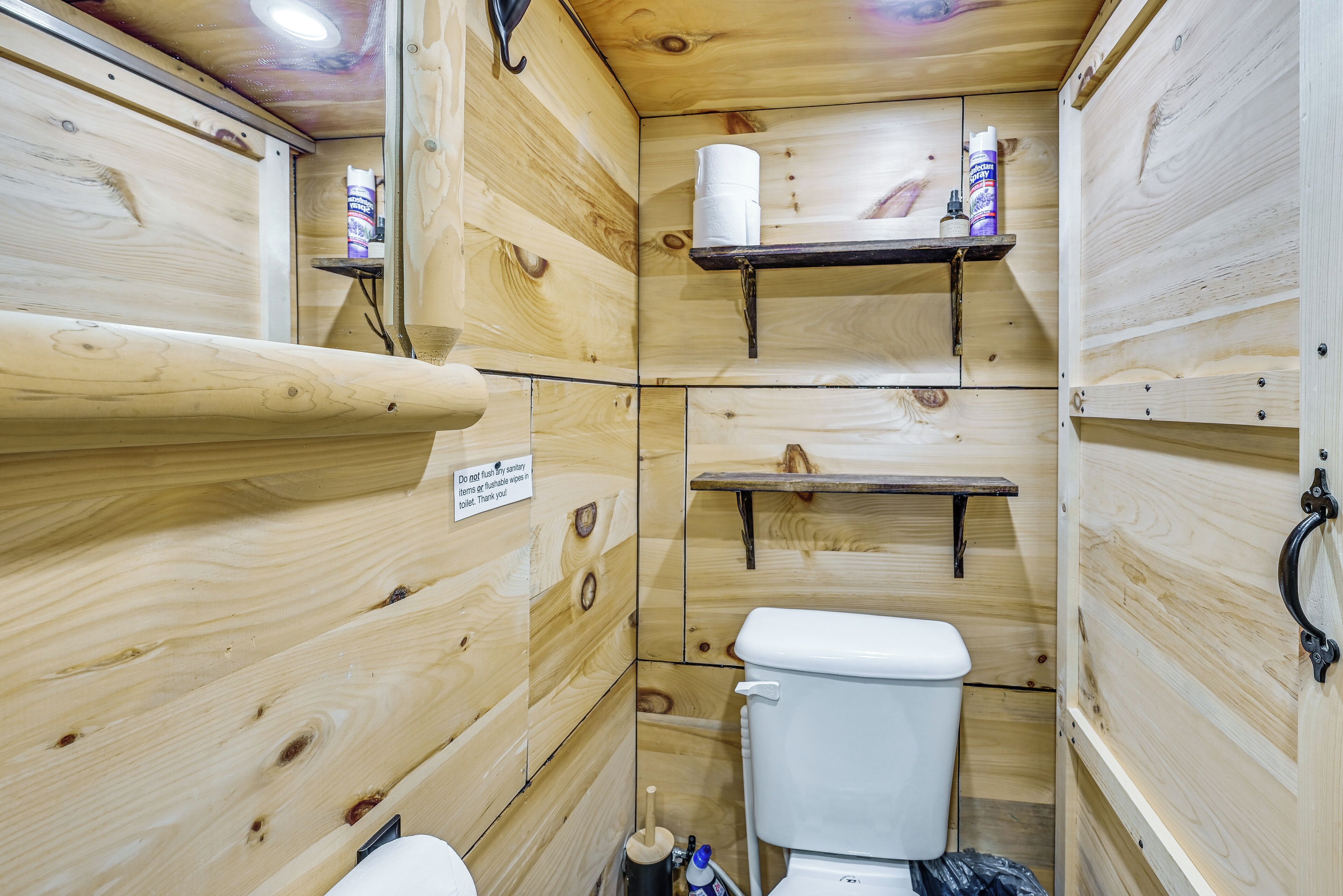 A wooden cabin-style bathroom with a toilet, shelves, and a sign.
