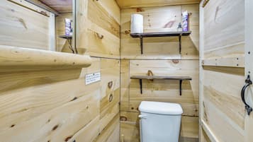 A wooden cabin-style bathroom with a toilet, shelves, and a sign.