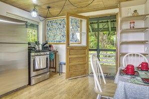 Una cocina con refrigerador, estufa y mesa de madera con tazas rojas.